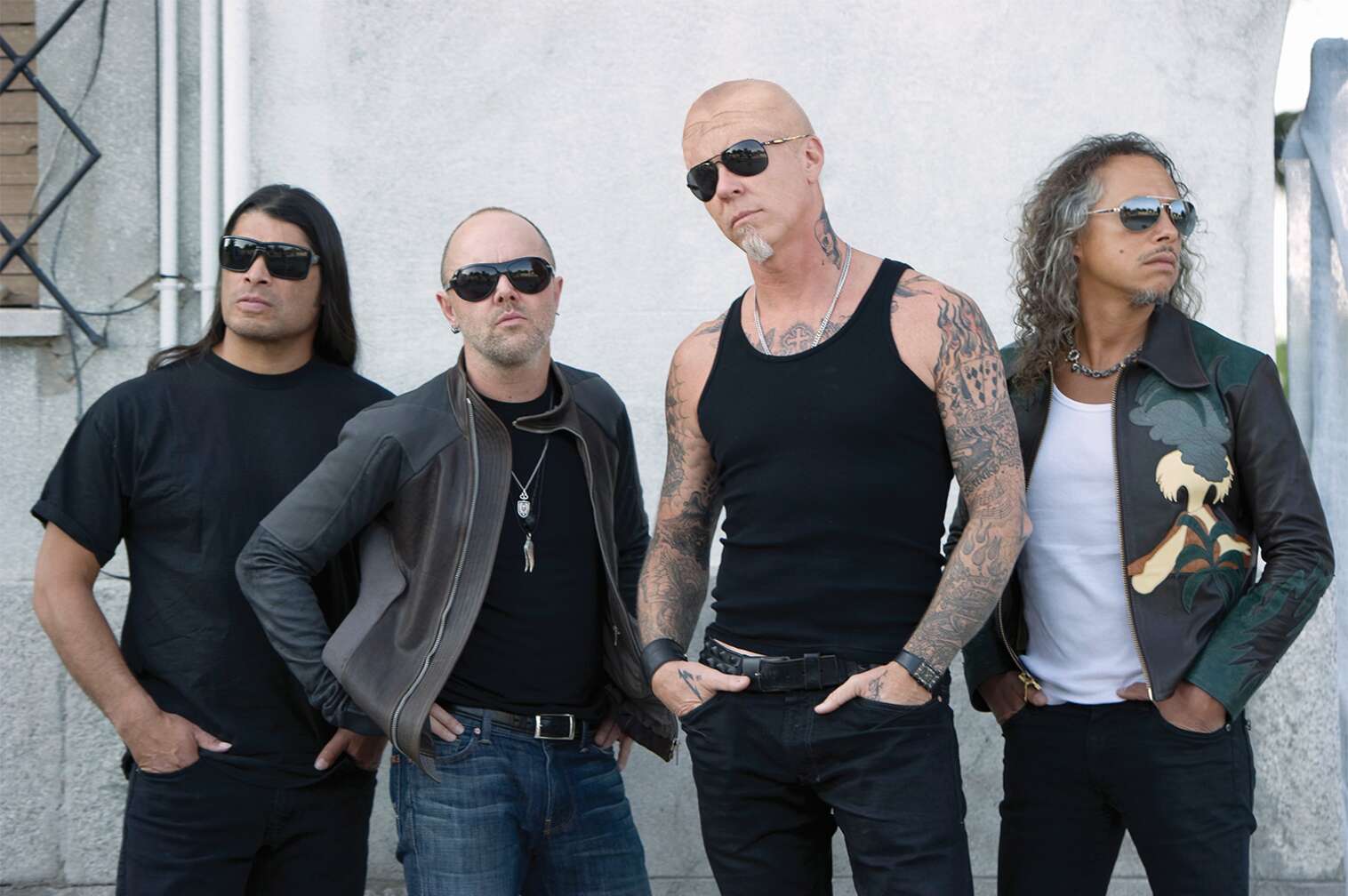 Metallica posieren nebeneinander vor einer weißen Hauswand