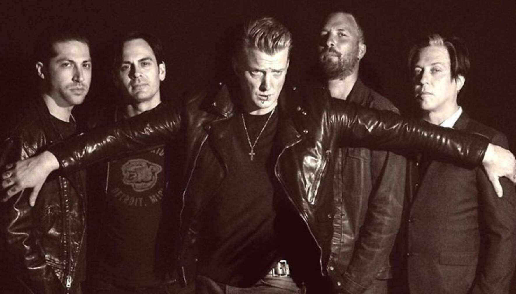 Josh Homme hält seine Arme vor die anderen Bandmitglieder von