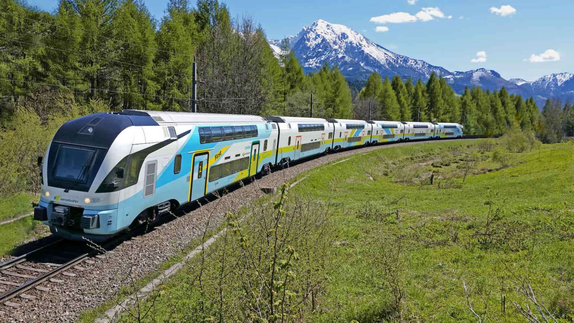 ein Zug der WESTbahn vor einem Hintergrund mit Bäumen und Wiese