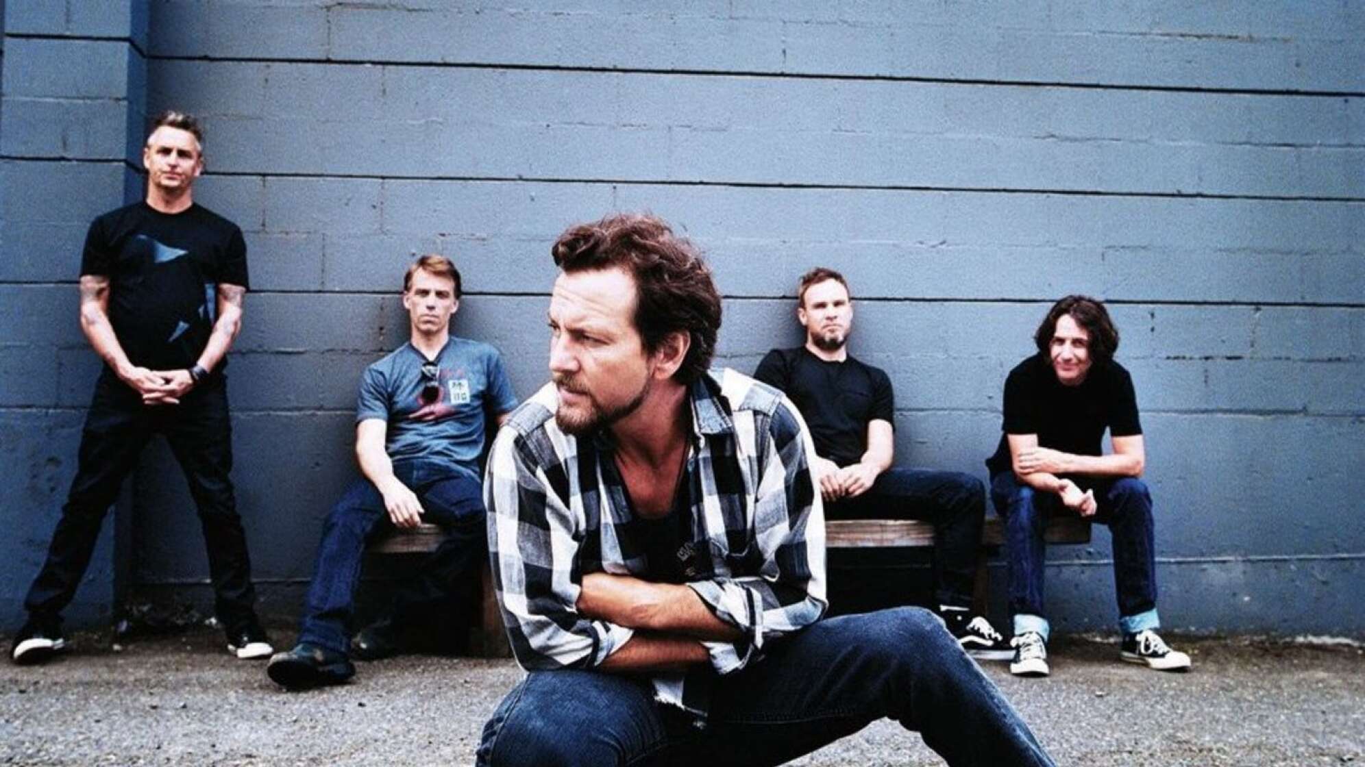 Pearl Jam posieren kniend und sitzend vor grauer Steinmauer