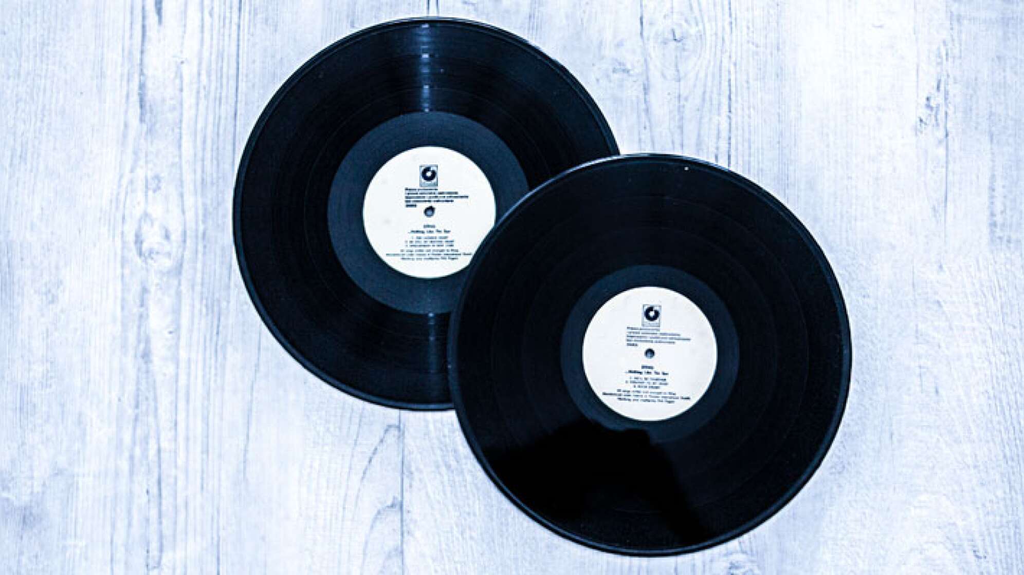 Zwei Schallplatten aufeinander vor einem weißem Holz Hintergrund