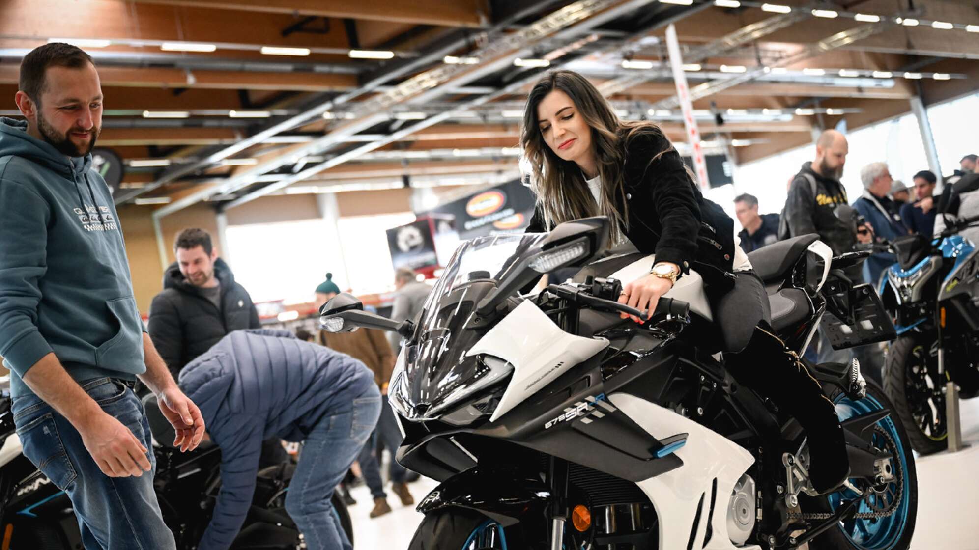 eine Frau mit langen schwarzen Haaren sitzt auf einem Motorrad in der Messehalle