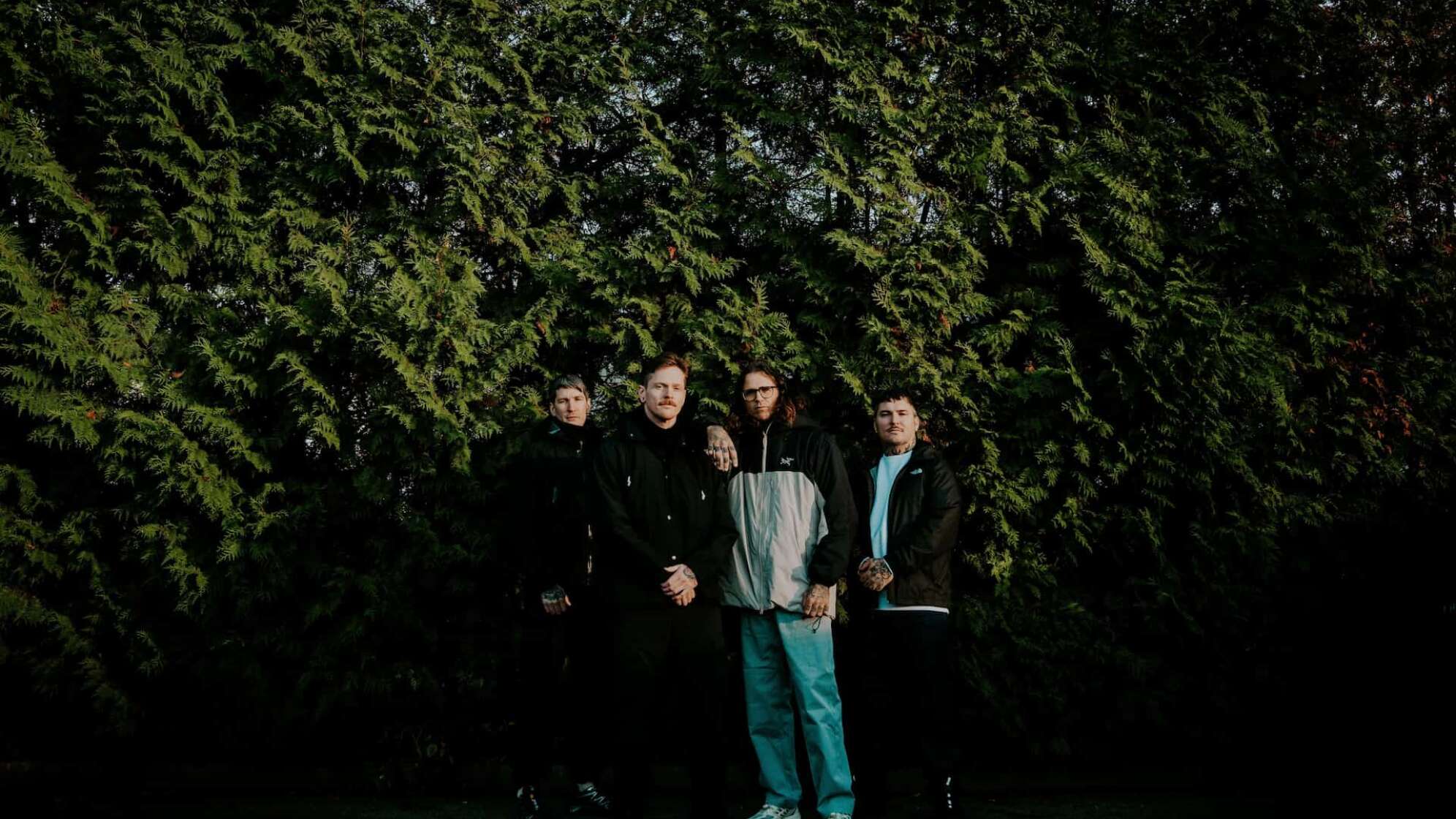 die Bandmitglieder von The Amity Affliction stehen vor einer Pflanzenwand