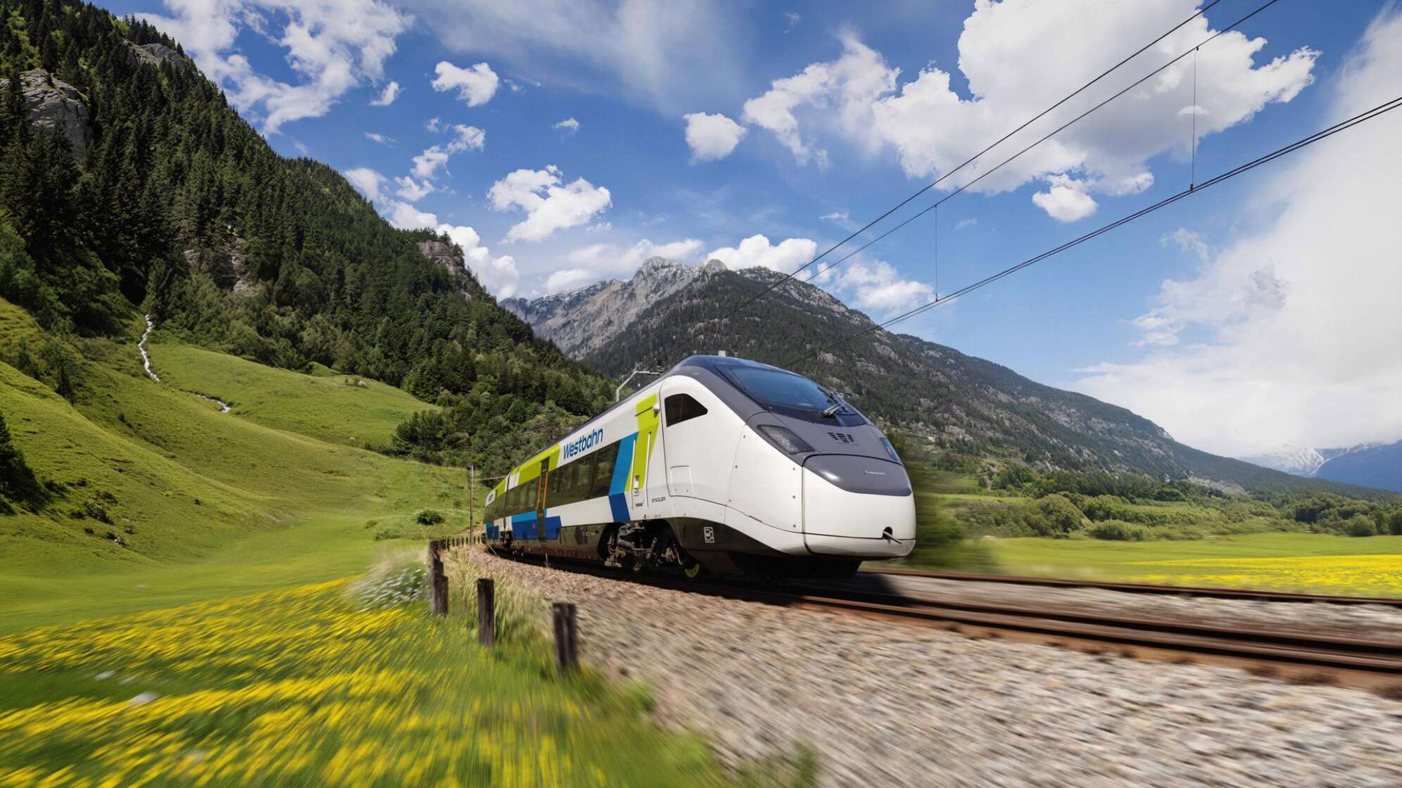 ein Zug der WESTbahn vor einem Hintergrund mit Bäumen und Berg