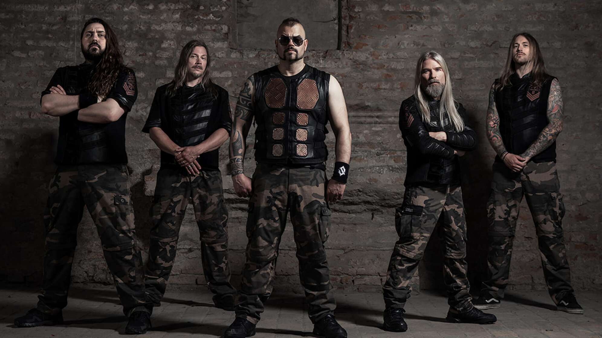 die fünf Bandmitglieder von Sabaton stehen vor einer grauen Wand