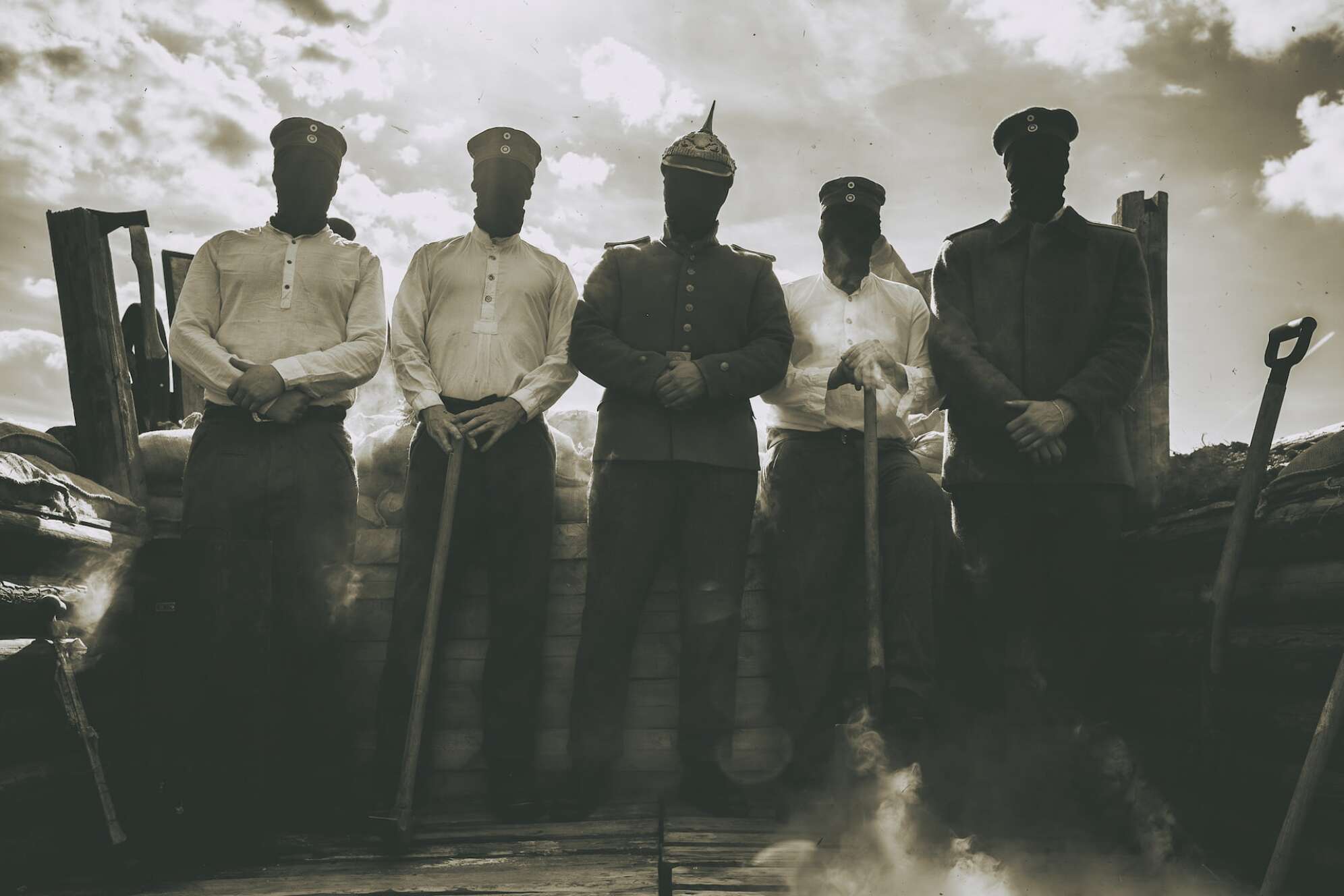 die fünf Mitglieder von Kanonenfieber in Uniformen des 1. Weltkriegs vor zwei Kanonen, über den Köpfen eine schwarze Haube, Foto in Schwarz-Weiß