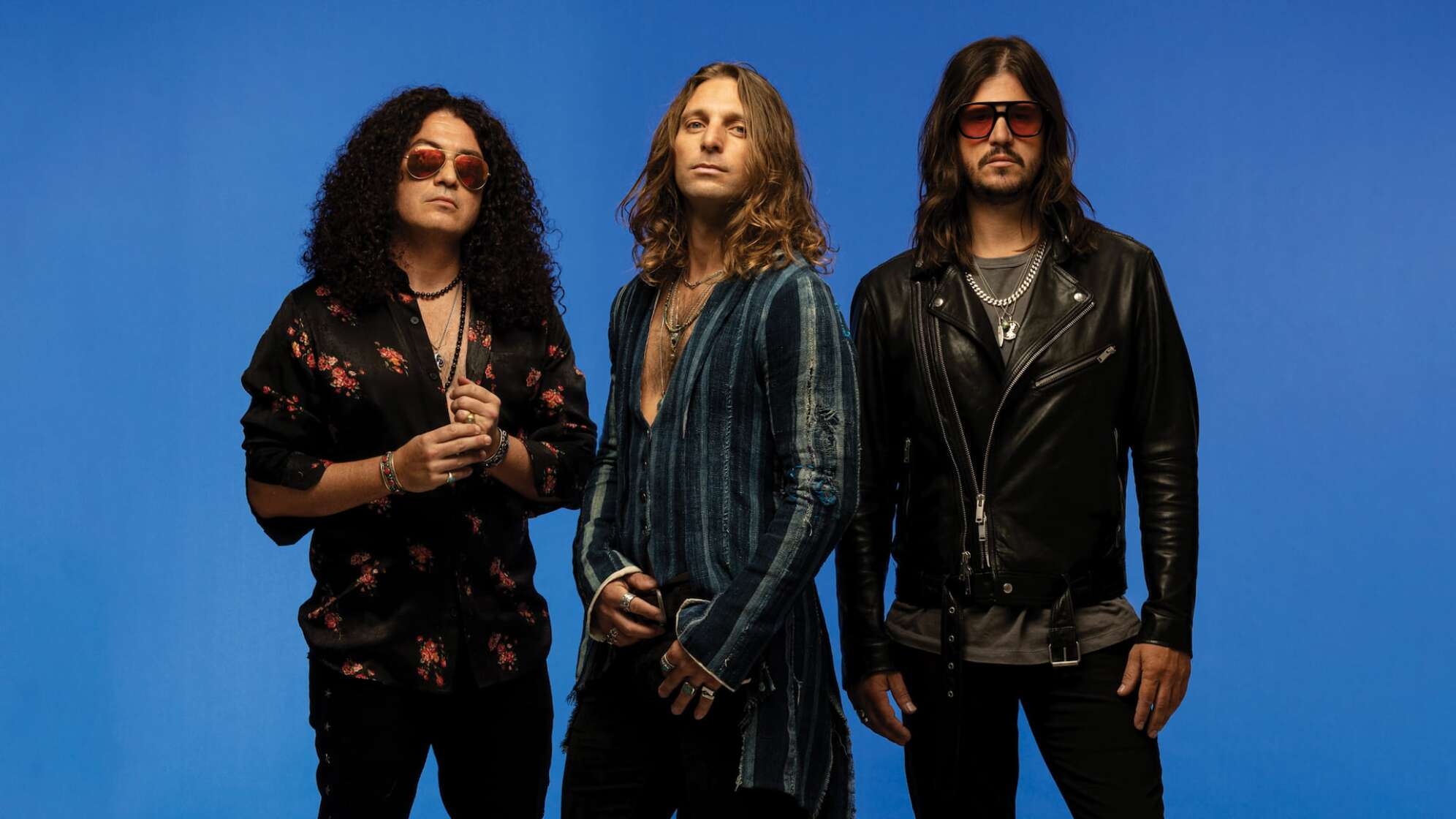 die drei Bandmitglieder von Dirty Honey vor einem blauen Hintergrund