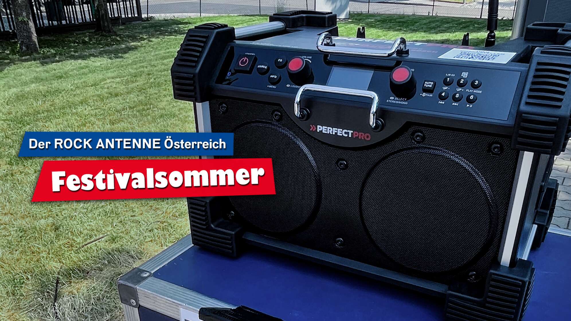 Ein DAB+ Baustellenradio des Modells "RockHart 18V" von PerfectPro auf einem Tisch im Freien, Aufschrift: "Der ROCK ANTENNE Österreich Festivalsommer"