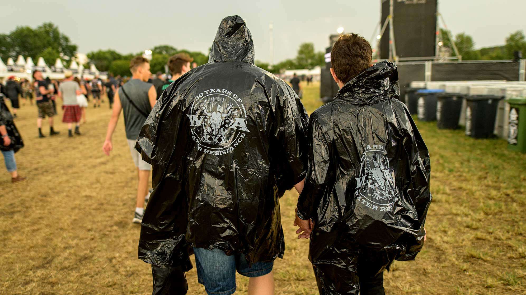 Zwei Besucher des Wacken Open Airs auf dem Festival-Gelände mit einem schwarzen Regen-Poncho.