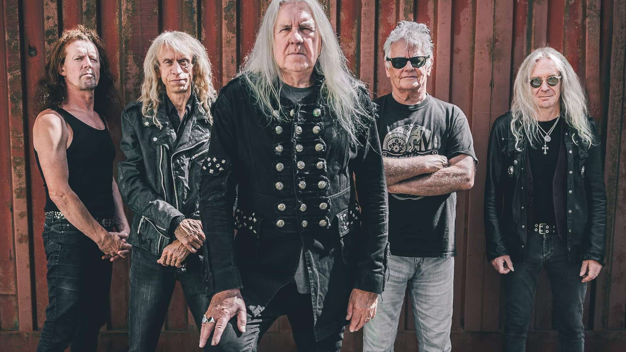Die Bandmitglieder von Saxon vor einer Holzwand